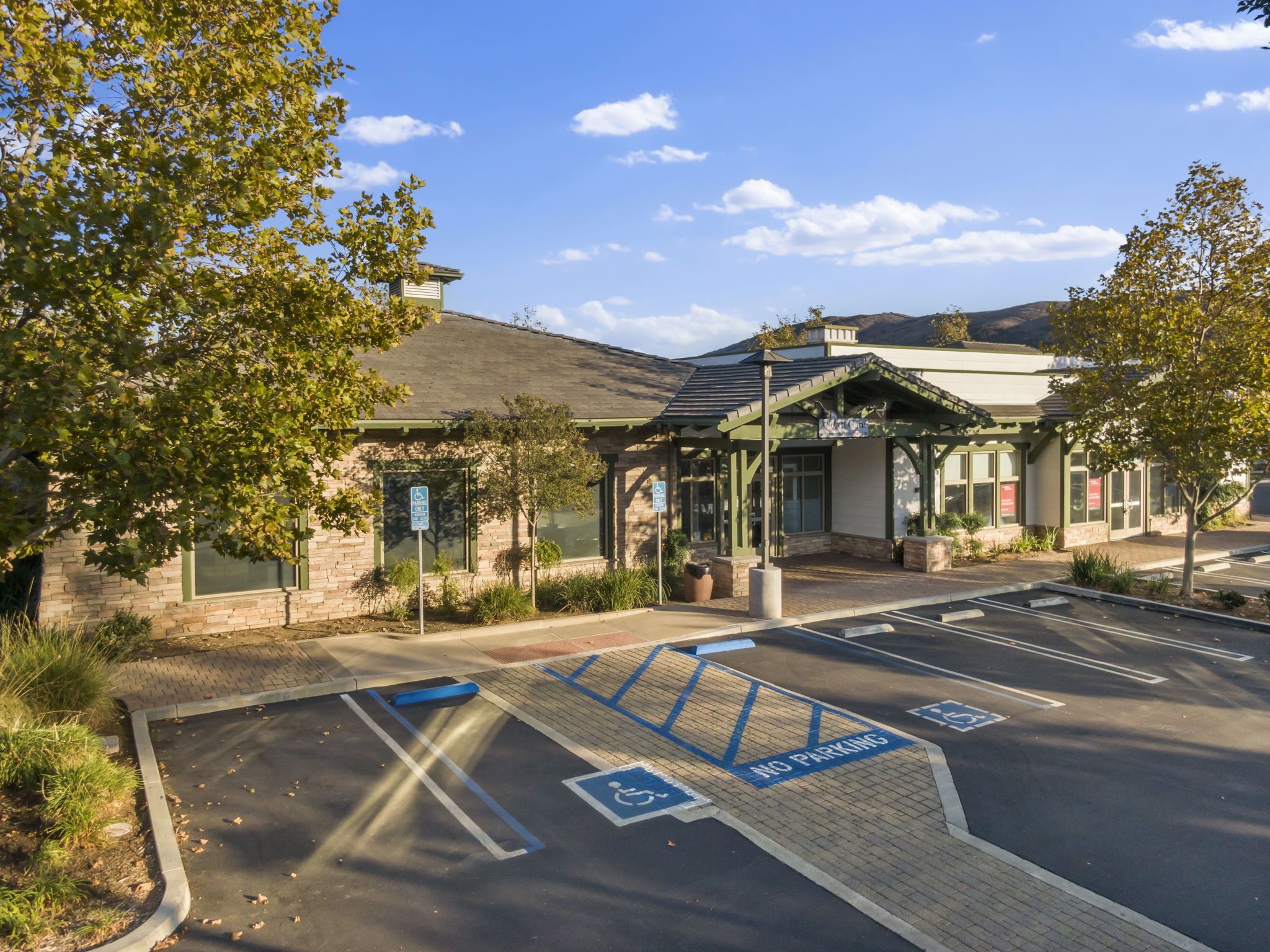 Stone-clad Craftsman storefronts of The Shops at Oak Creek with mature trees and parking